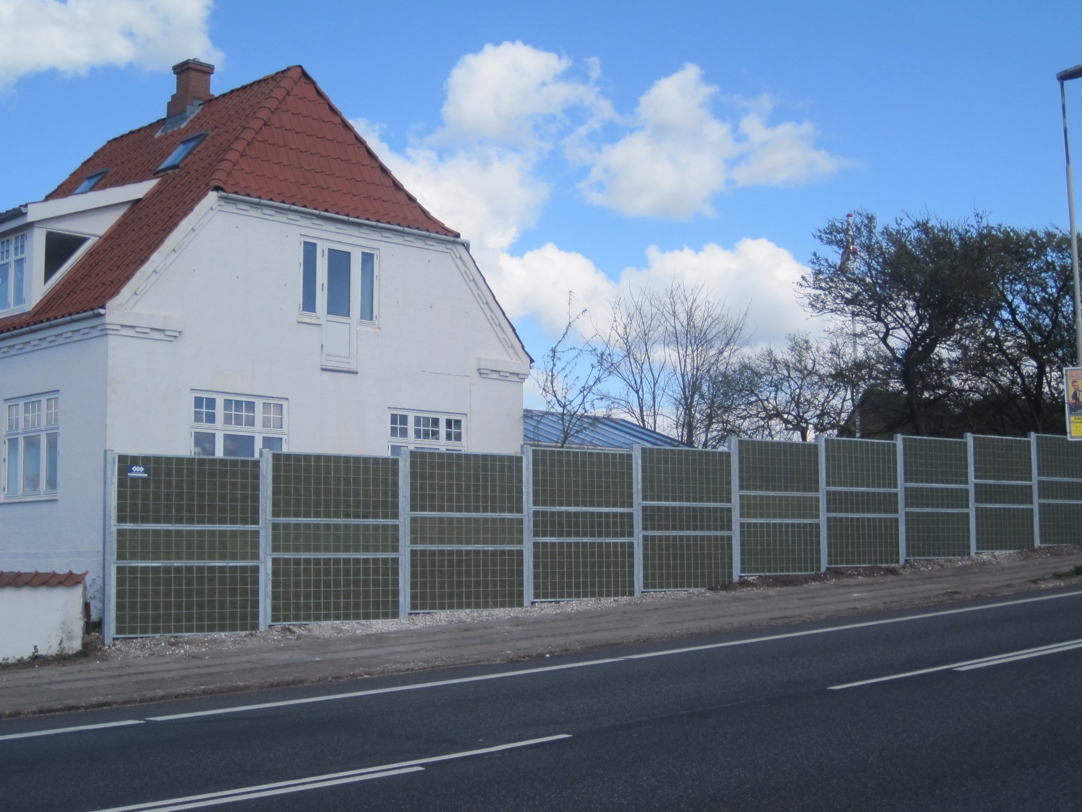 Ett Noistop® Steel bullerplank från Poda Stängsel monterat framför ett hus för att absorbera och skärma av från ljudet från trafiken.
